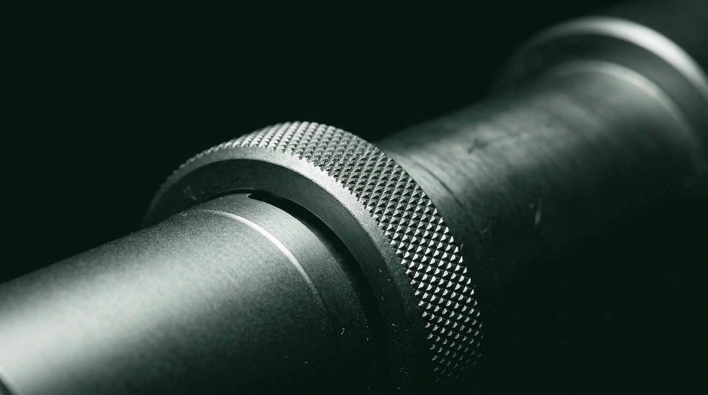 Macro of a knurled precision adjustment dial on dark instrument metal with green-black reflections