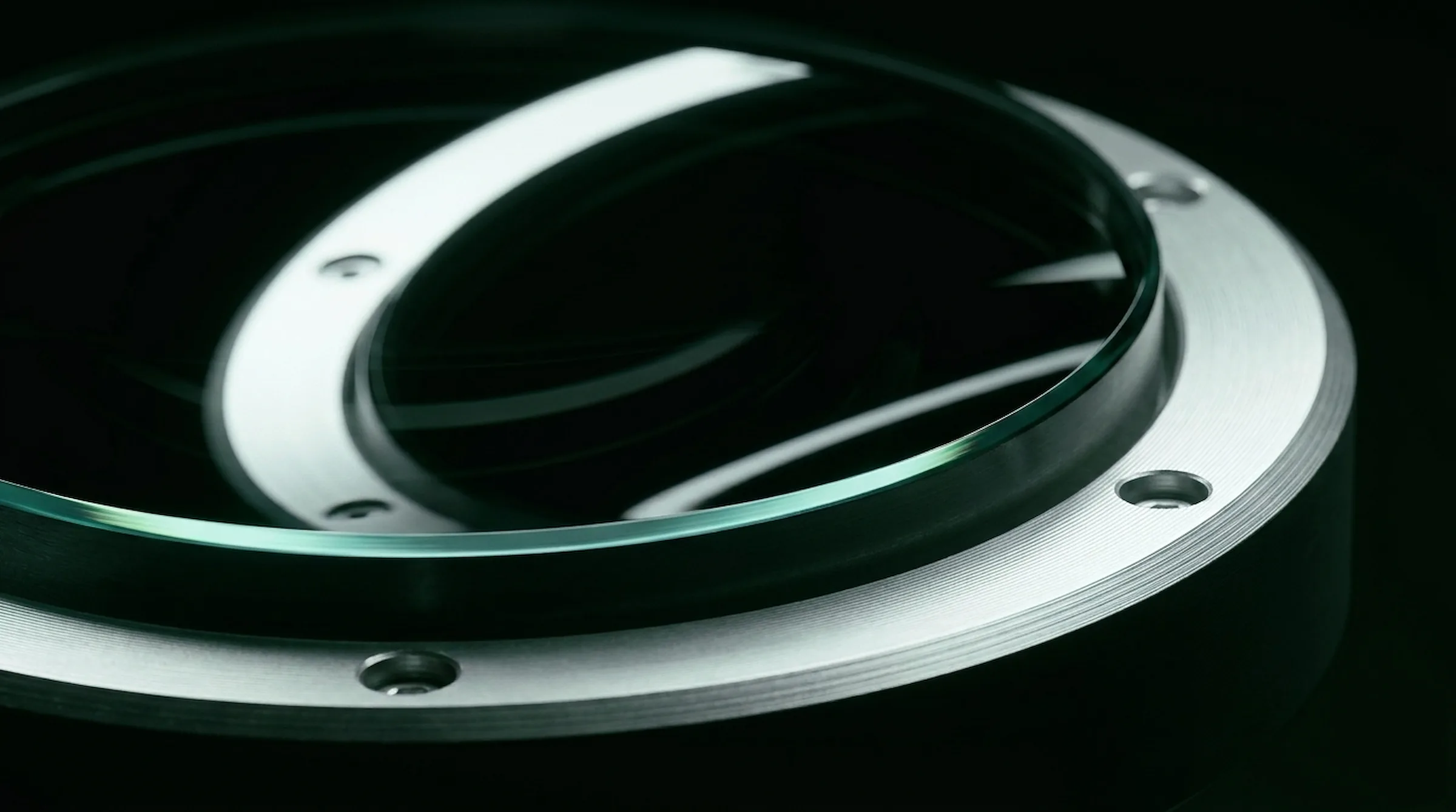 Macro of a dark glass instrument lens in a brushed metal ring with green-black reflections