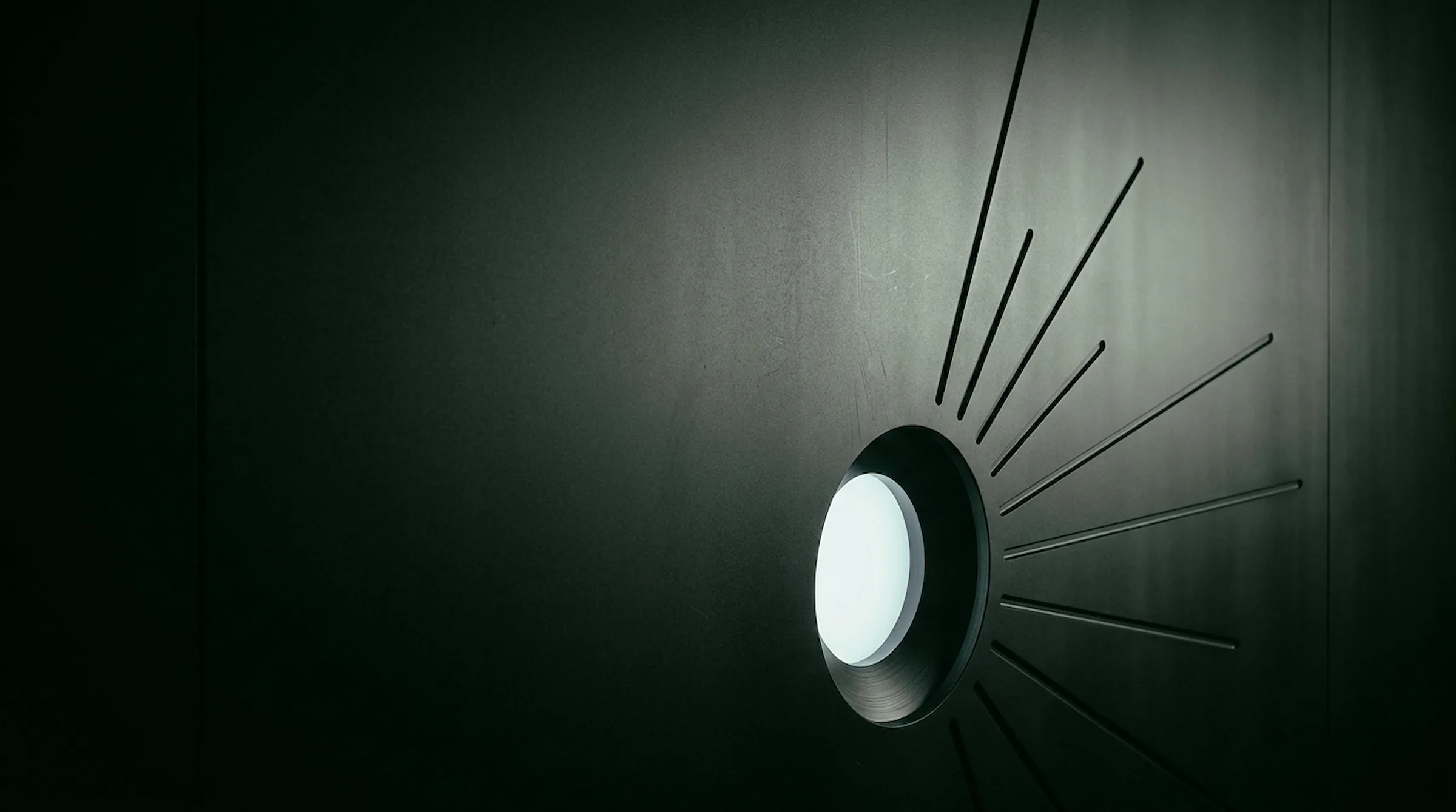 A single glowing white aperture in a dark wall, radiating thin lines of light